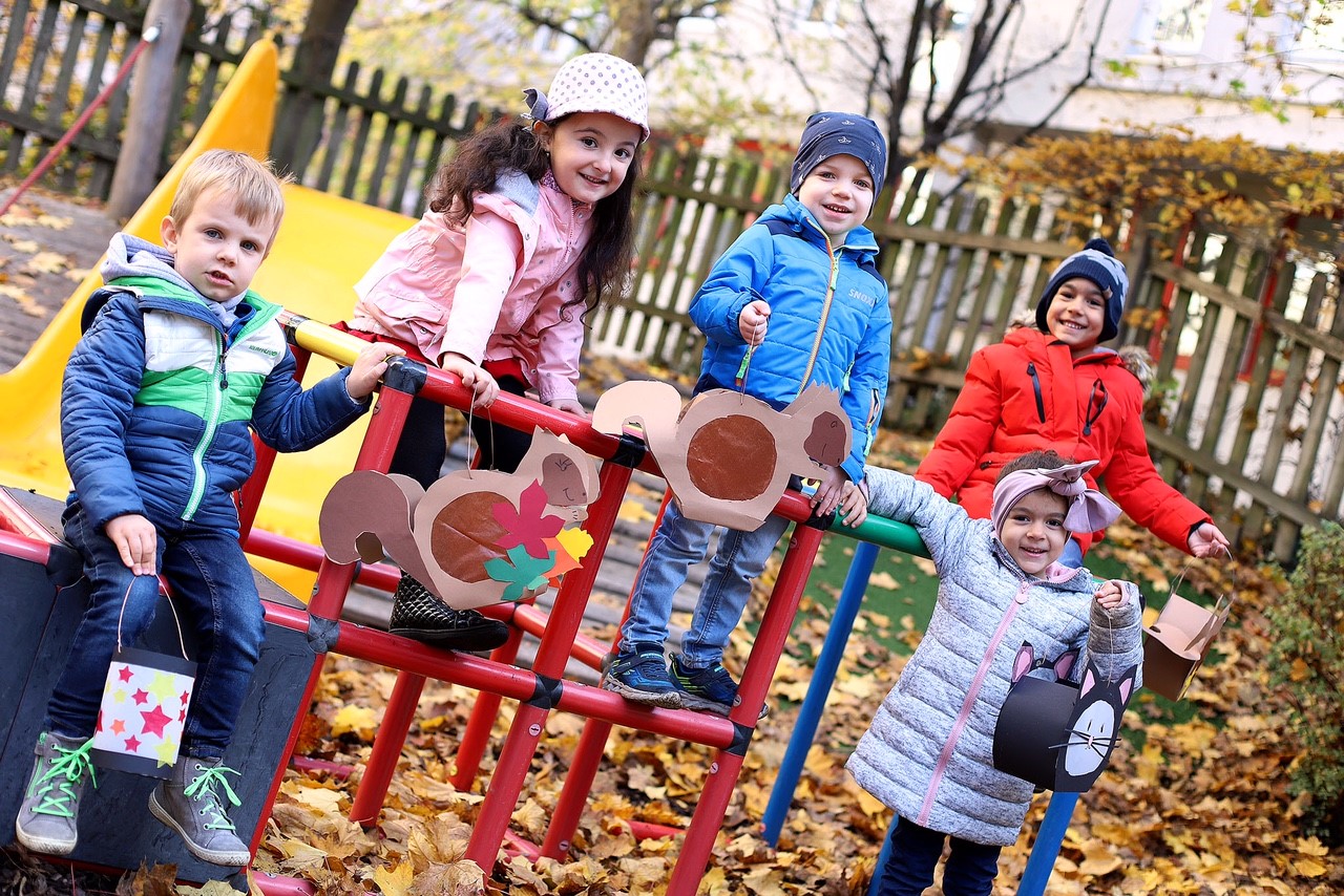 5 Kinder stehen im Garten um ein Klettergerüst und halten Laternen in ihren Händen